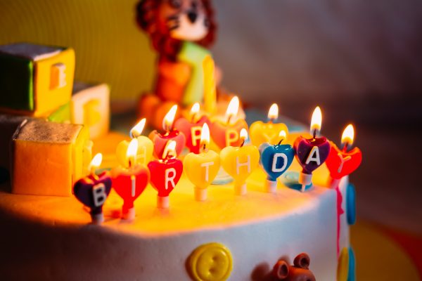 Happy Birthday Written In Lit Candles On Colorful Cake.