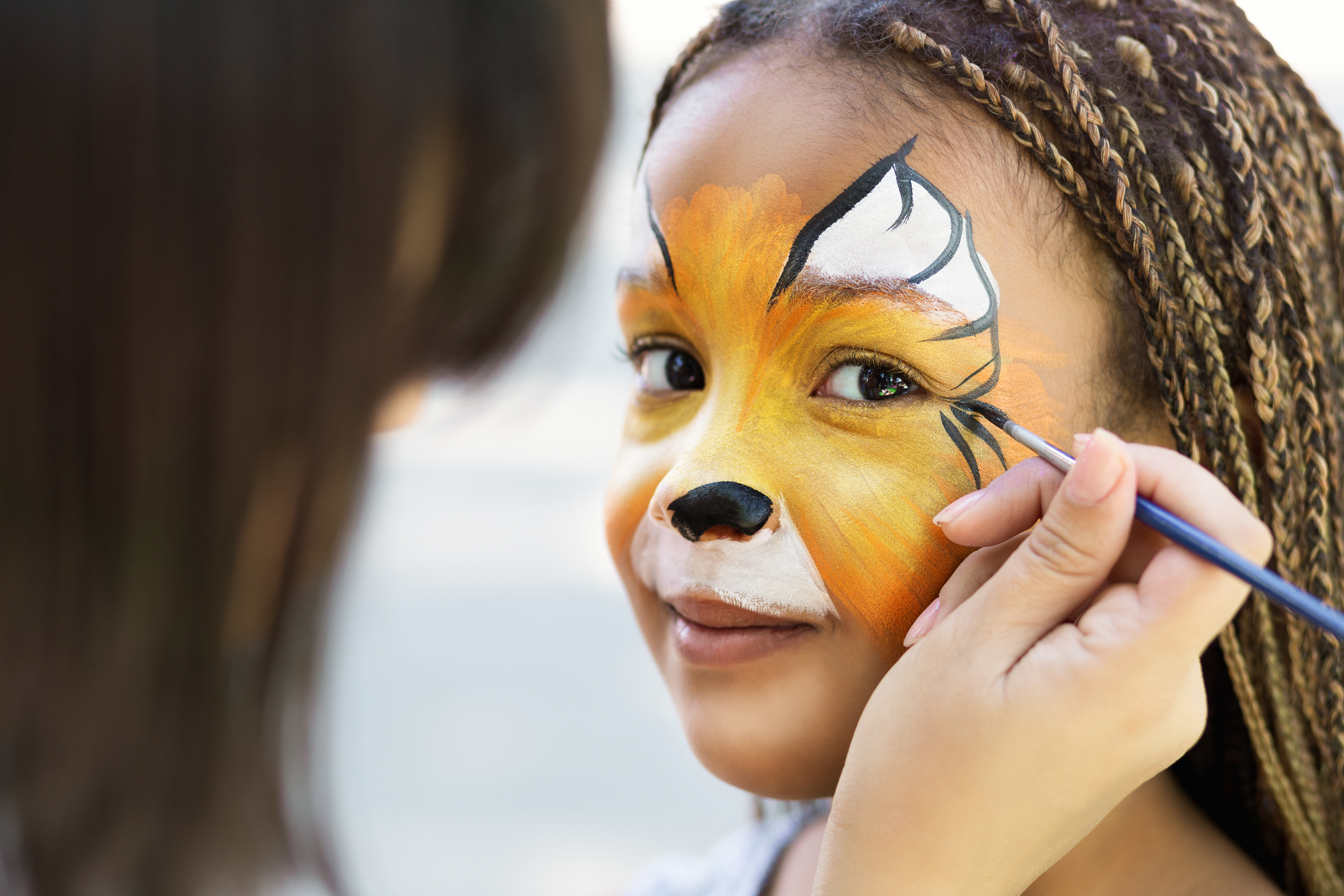 Children face painting. Artist painting little african-american girl like tiger, copy space